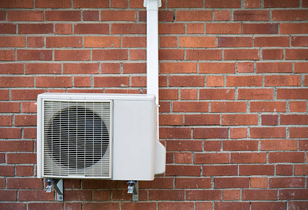 A heat pump sits agains the brick wall of a home.